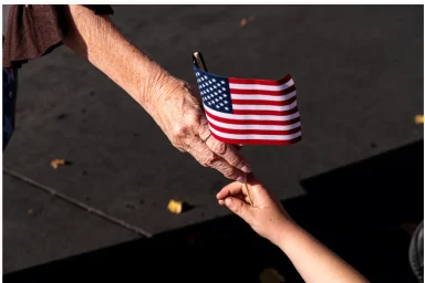 Close-up of an elderly hand passing a small American flag to a child