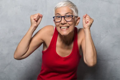 Older woman in a red tank top raising both fists in celebration