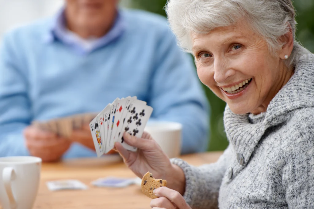 Older woman holding a hand of playing cards and a cookie outdoors