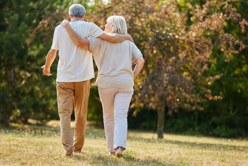 Older couple walking arm in arm away from the camera through a field