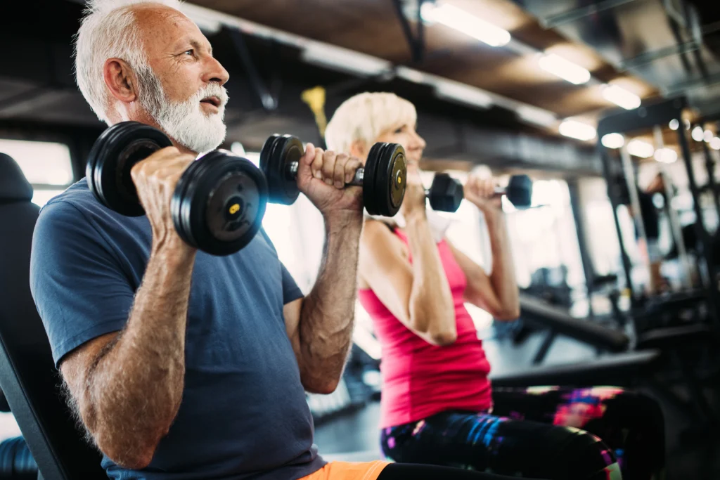Older man and woman lifting dumbbells together in a gym