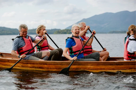 Group of older adults paddling a canoe on a lake, laughing together