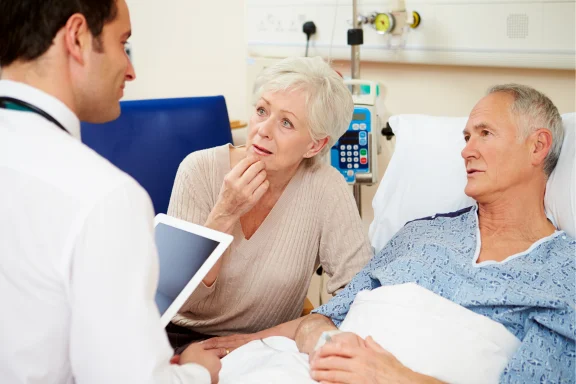 Doctor with a tablet consulting a woman beside a hospital patient's bed