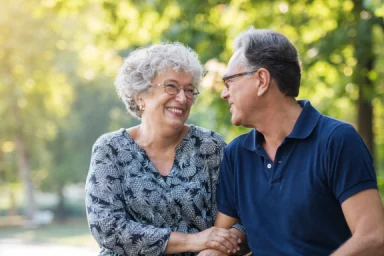 Older man and woman smiling face to face while holding hands in a park