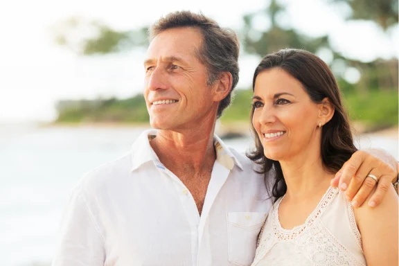 Mature couple in white outfits embracing on a beach