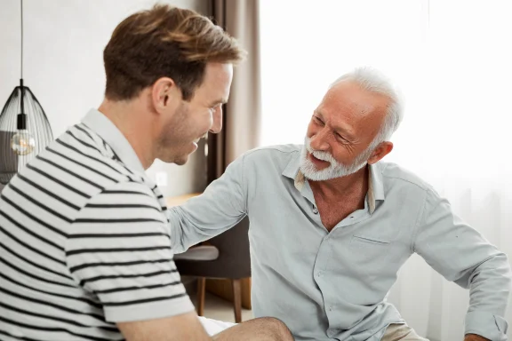 How to tell your kids you’re getting a reverse mortgage. Older man and a younger man sharing a laugh in conversation indoors