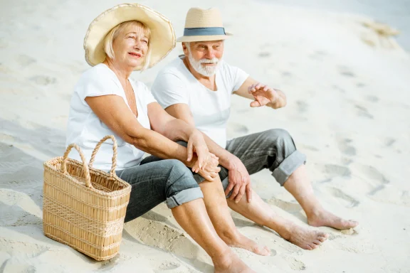 Older couple in sun hats sitting together on a sandy beach